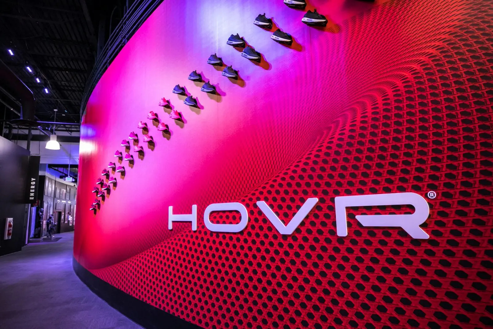 Under Armour showroom wall displaying rows of athletic shoes above a large HOVR logo in red and purple lighting