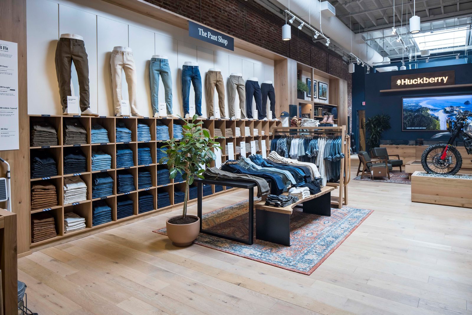 Huckberry store interior with The Pant Shop display, rows of folded pants, clothing racks, and a motorcycle display.