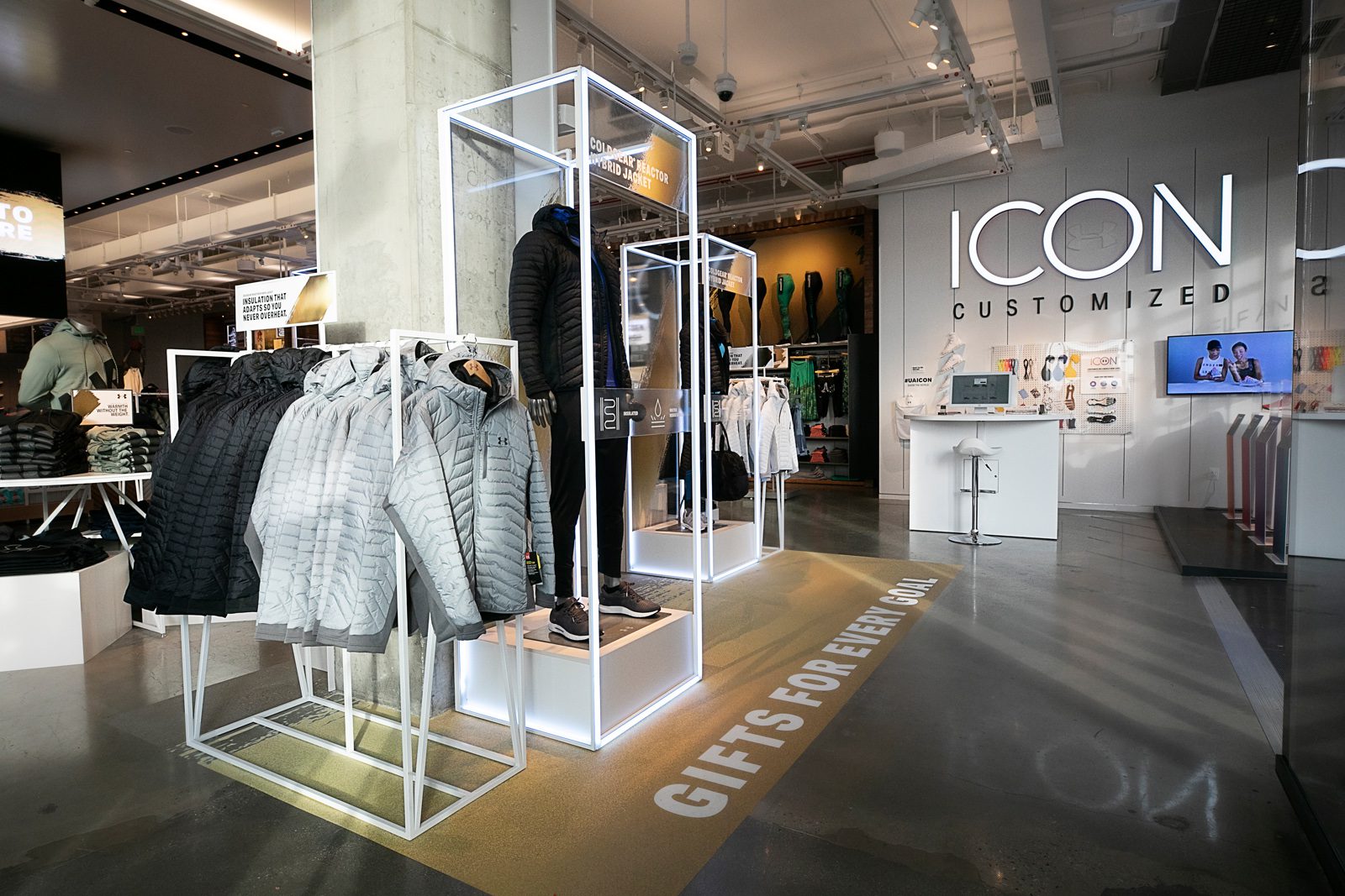 Interior of an Under Armour store with quilted jackets, apparel displays, and an ICON Customized service counter.