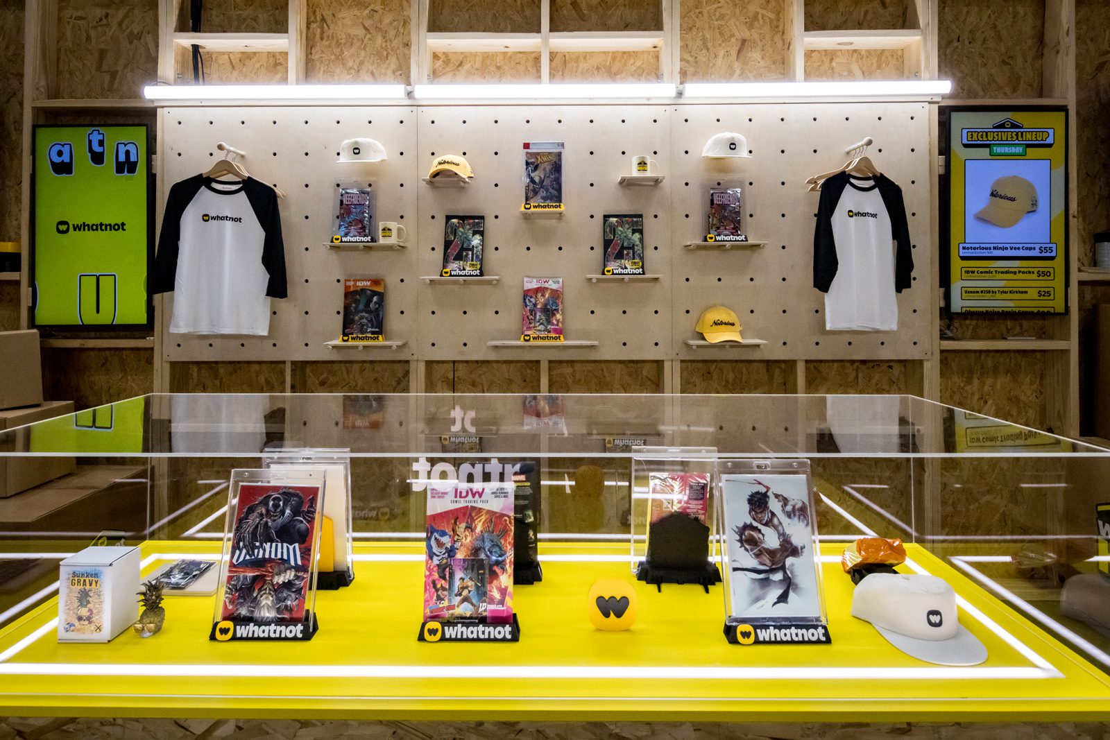 Whatnot merchandise display featuring comic books, branded shirts, caps, mugs, and other collectibles.