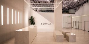 Minimalist Zensai reception interior with a white desk, geometric benches, vertical wall lights, and patterned ceiling installation