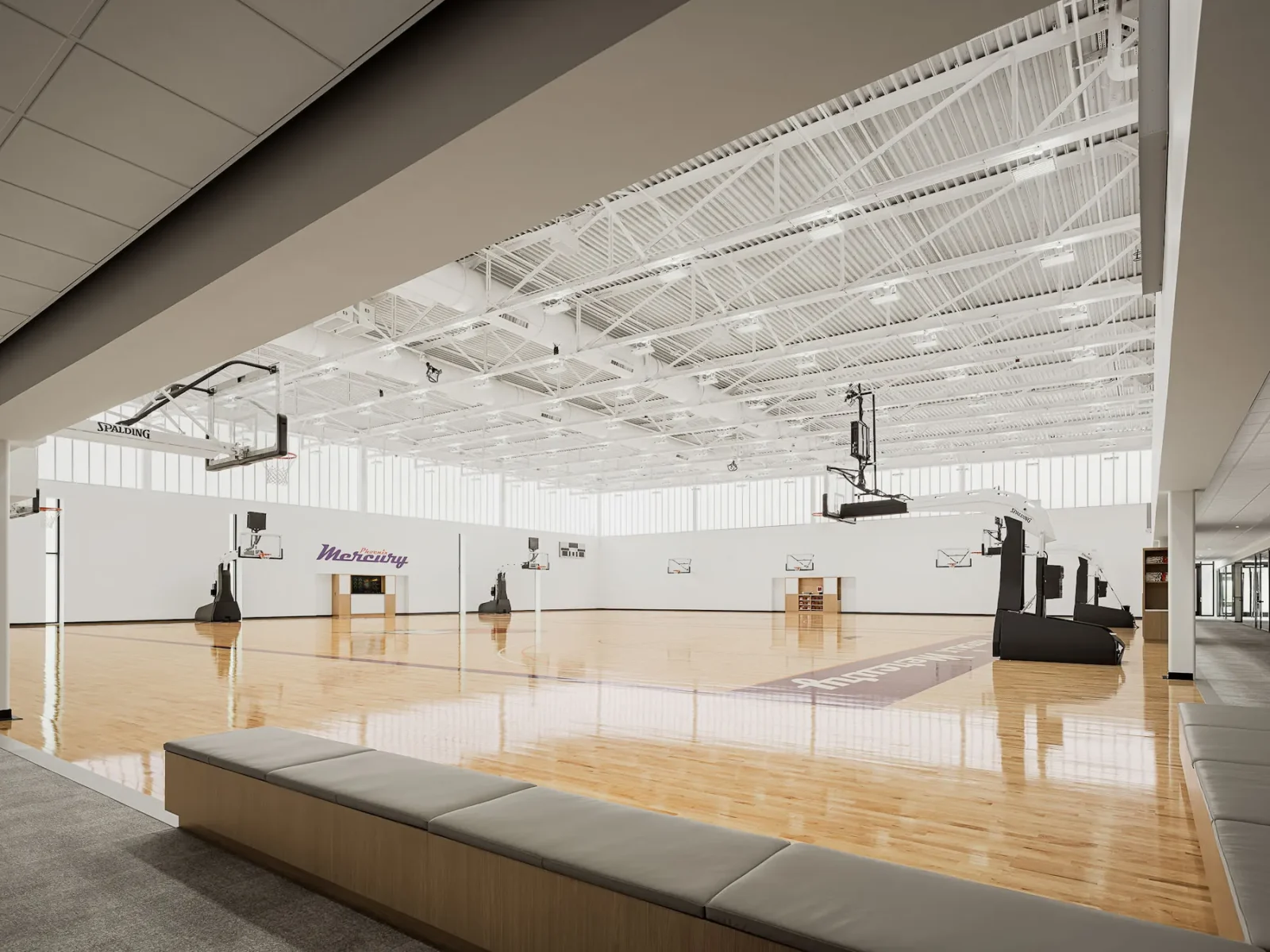 Indoor basketball practice facility with multiple courts, hoops, polished wood floors, and Phoenix Mercury logo on the wall