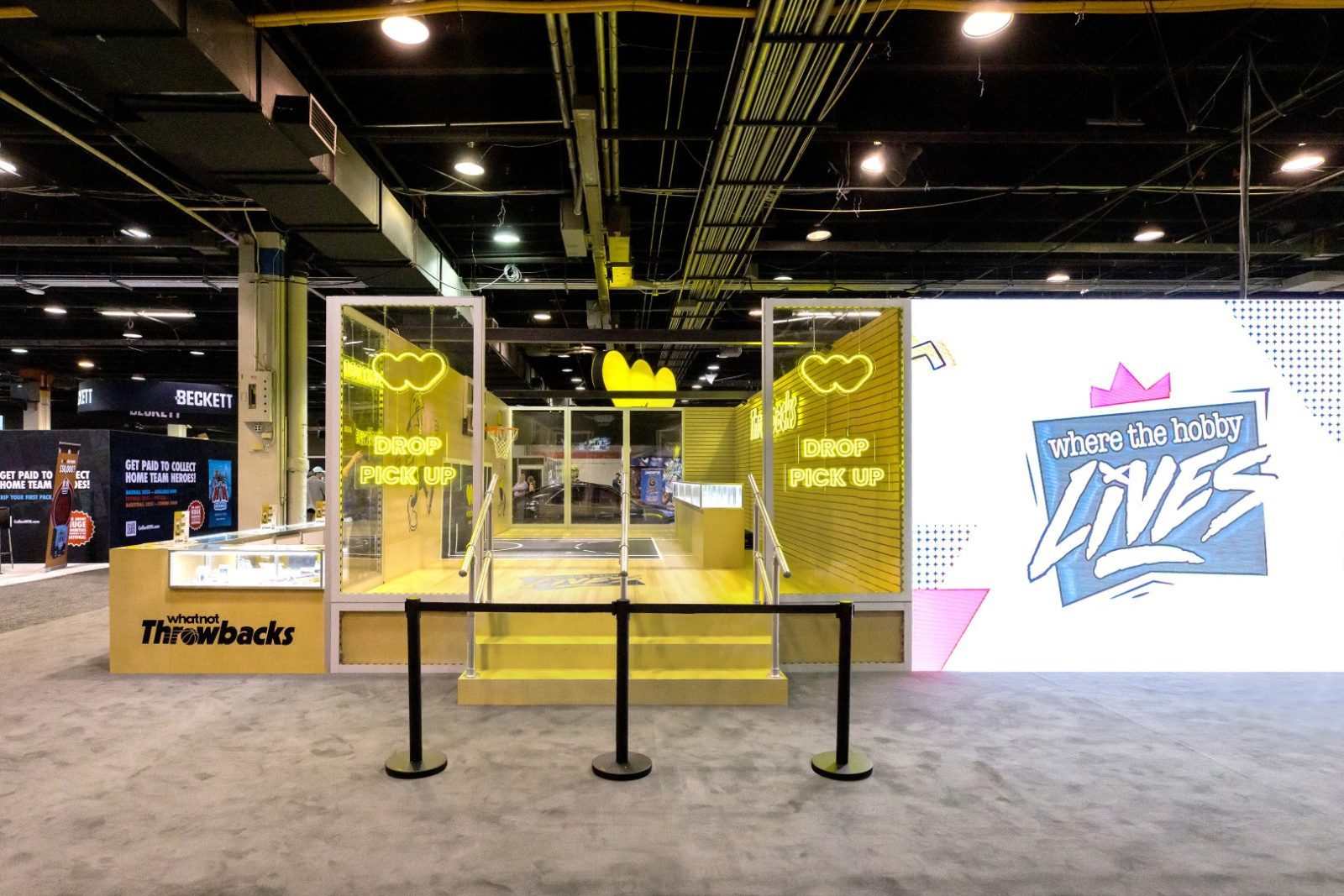 Whatnot Throwbacks booth with neon “Drop Pick Up” signs and a large “Where the hobby lives” display in an event hall.