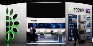 Shoals exhibition booth displaying branded electrical equipment, digital panels, and a glowing green logo while attendees walk through