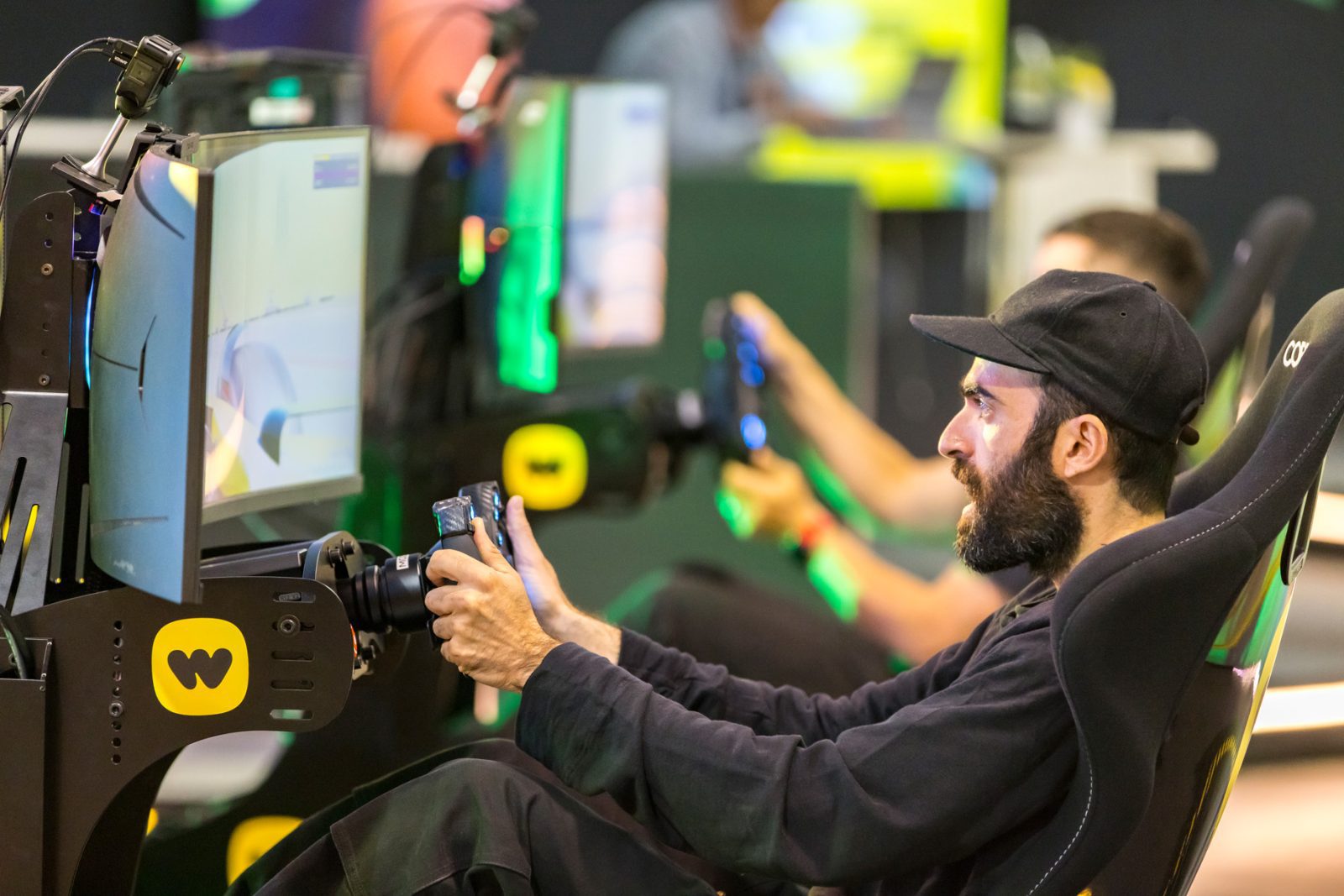 Man wearing a black cap using a racing simulator with a steering wheel and monitor setup