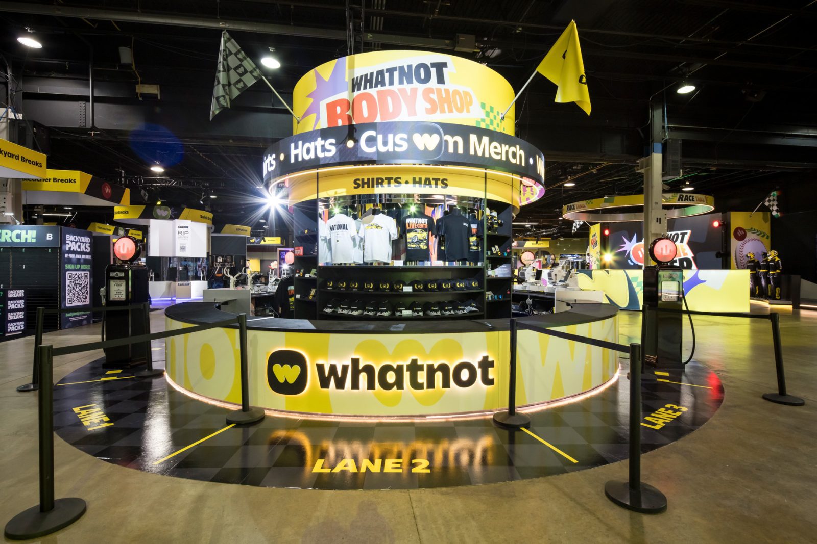 Whatnot Body Shop merchandise booth displaying shirts and hats at a brightly branded event venue