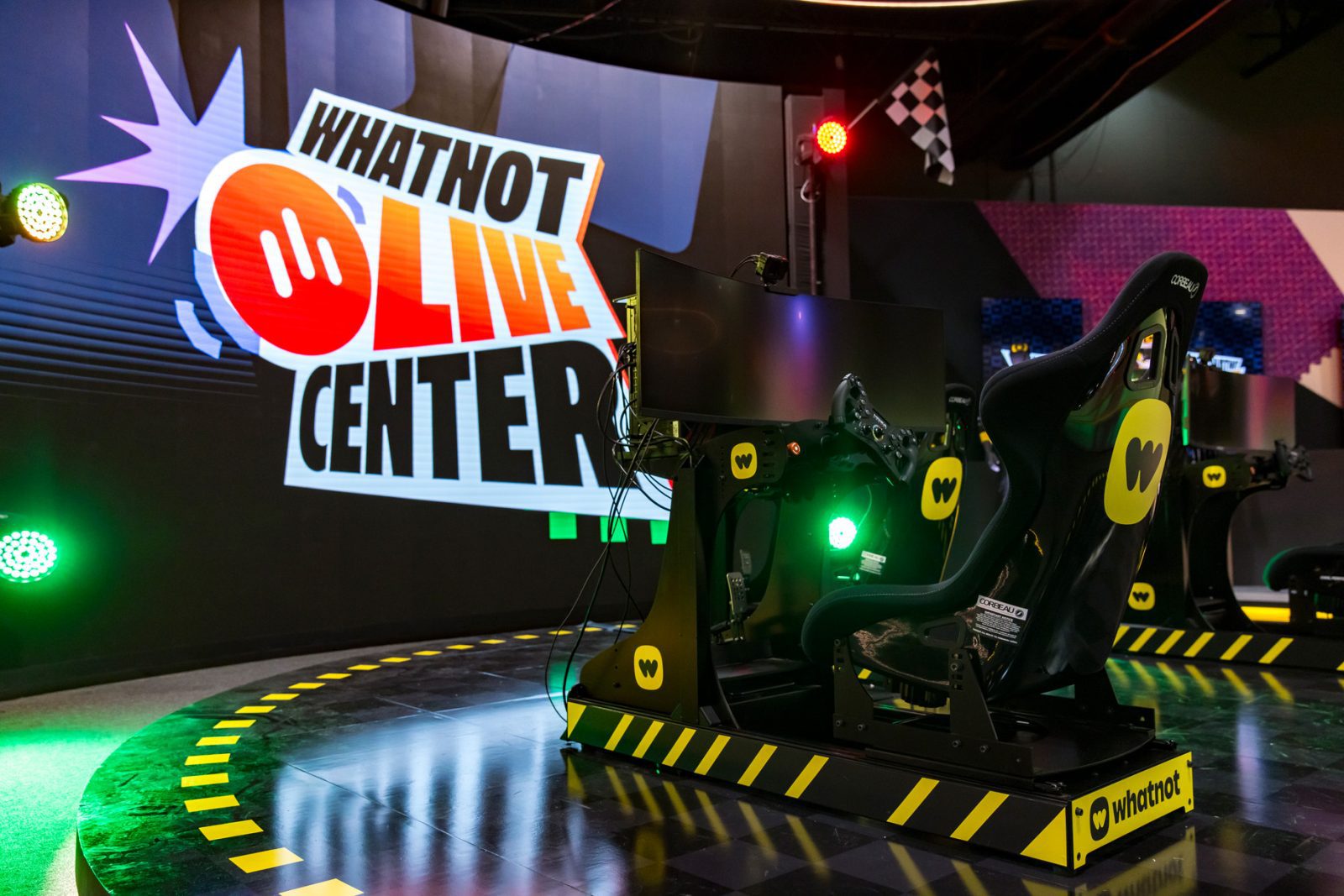 Whatnot Live Center sign behind a branded racing simulator setup with monitors, cockpit seats, and colorful stage lighting