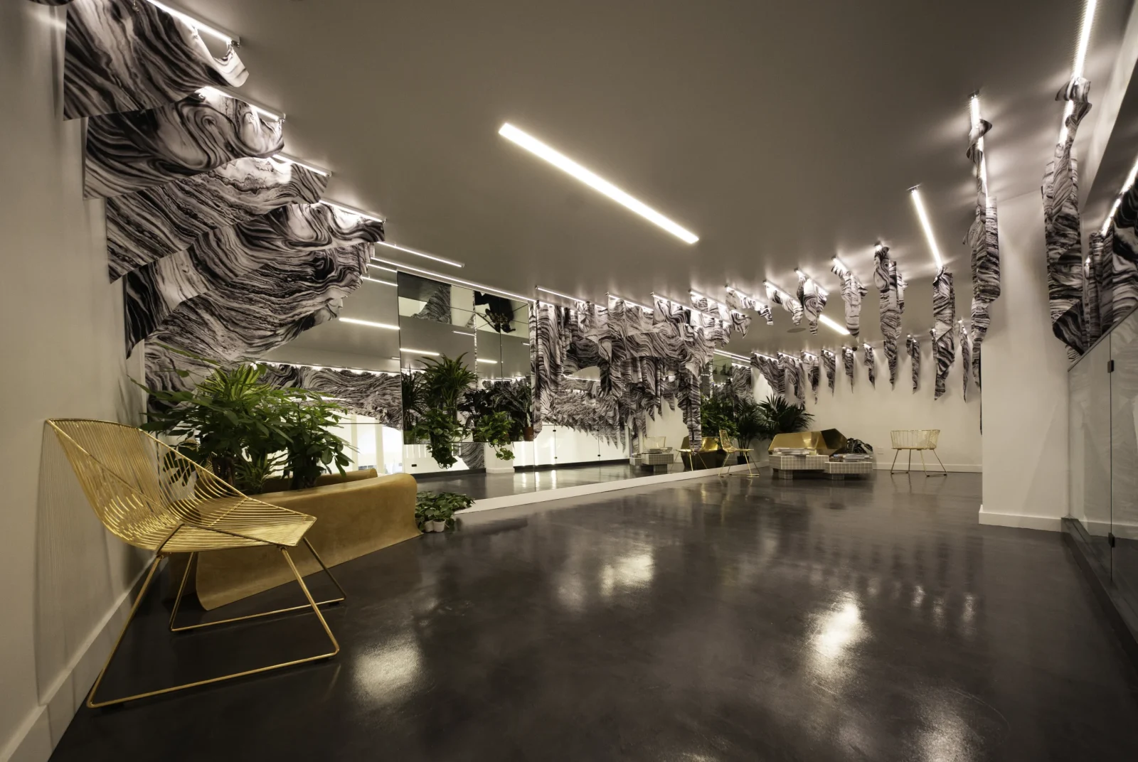 Modern lobby with black-and-white marbled wall art, mirrored panels, indoor plants, lounge seating, and polished dark flooring.