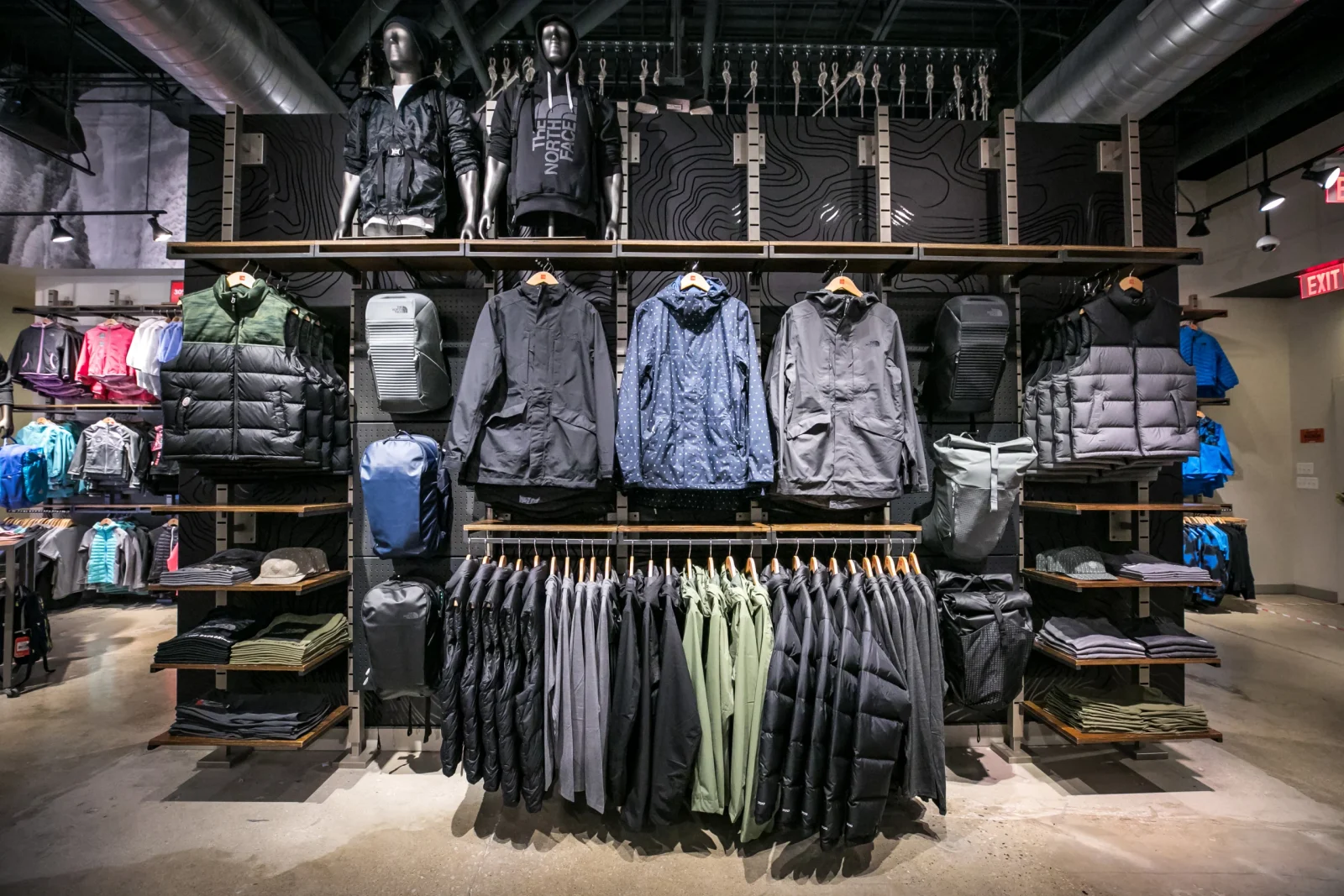 The North Face store display with mannequins, jackets, vests, backpacks, and folded clothing.