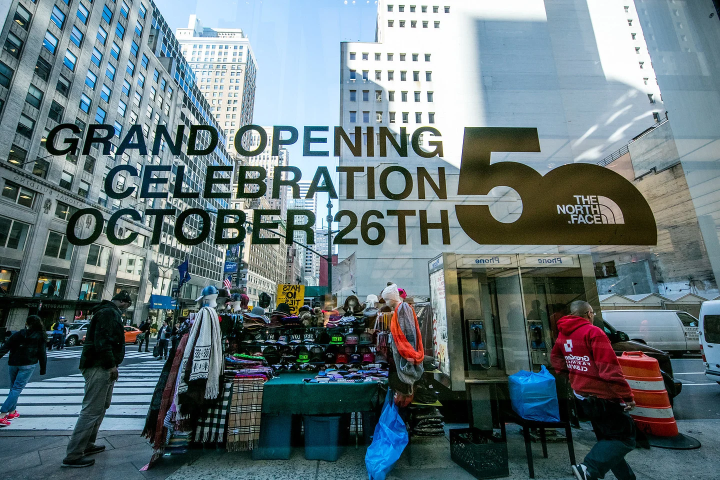 The North Face storefront window announcing a grand opening celebration on October 26th, viewed on a busy city street.