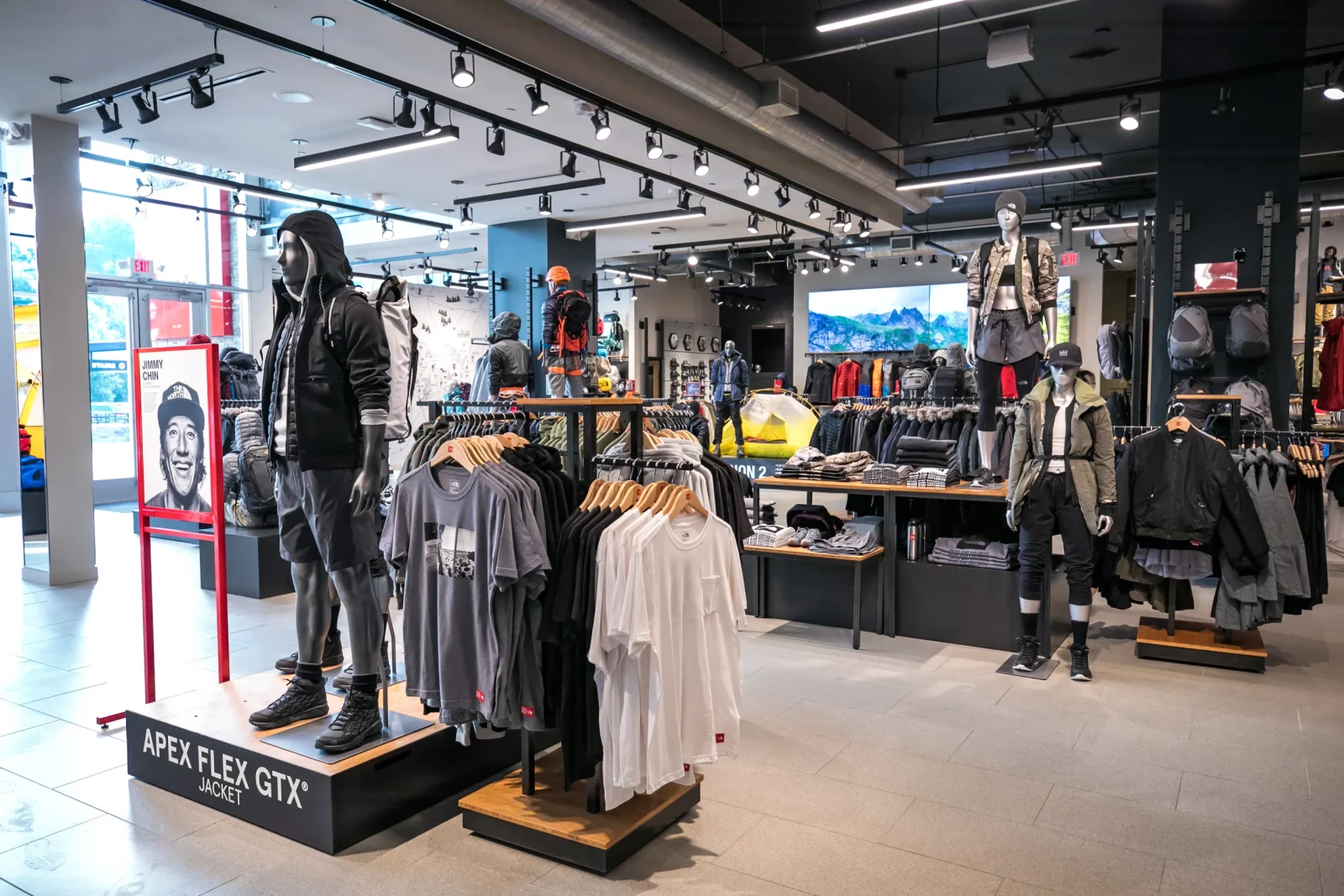 Interior of an outdoor apparel store with mannequins, clothing racks, backpacks, and an Apex Flex GTX jacket display