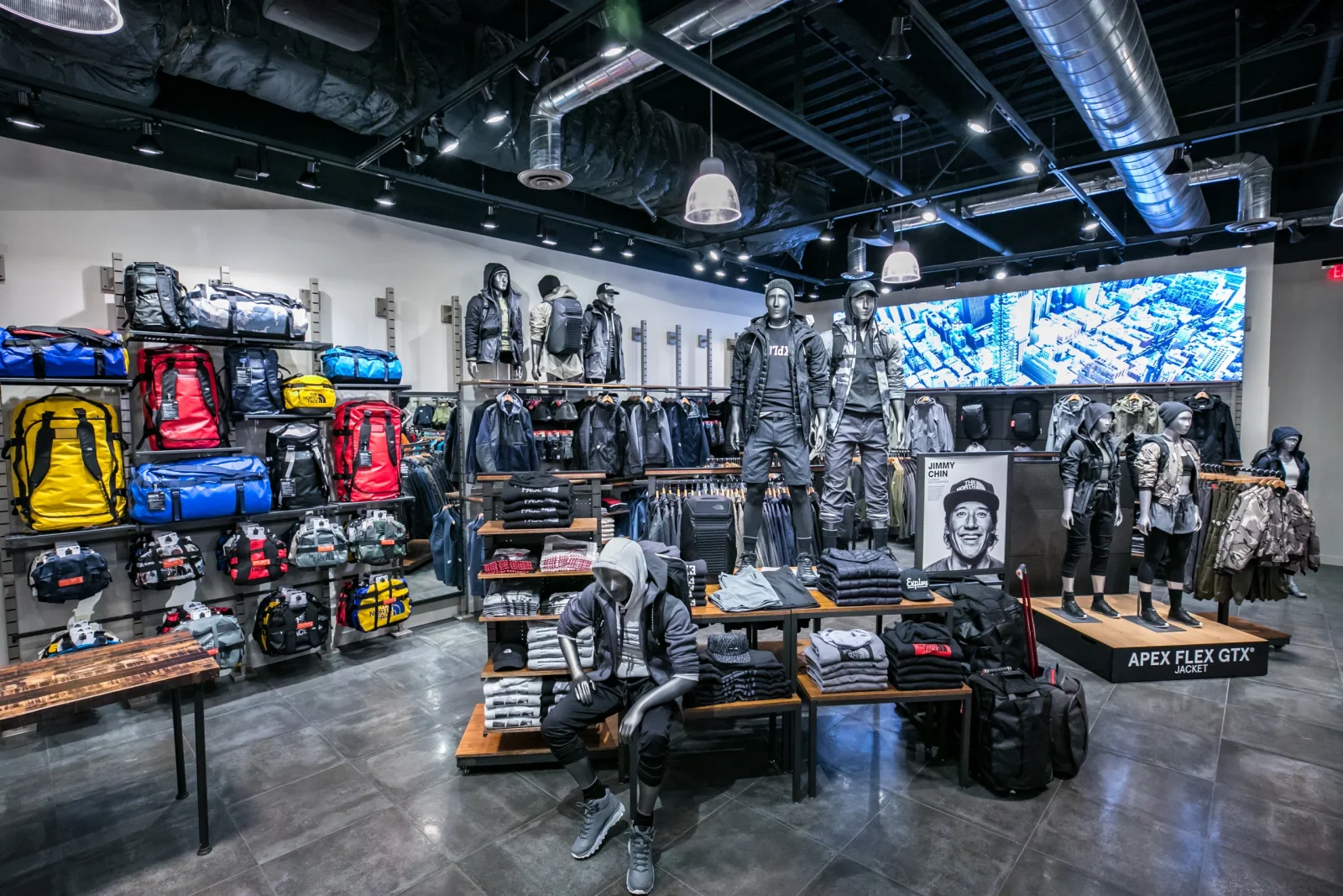 Interior of a The North Face store displaying outdoor clothing, backpacks, mannequins, and a Jimmy Chin poster.