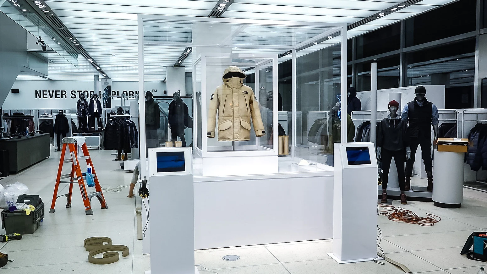 The North Face store interior with a tan parka in a glass display, mannequins, clothing racks, and “NEVER STOP EXPLORING” signage.