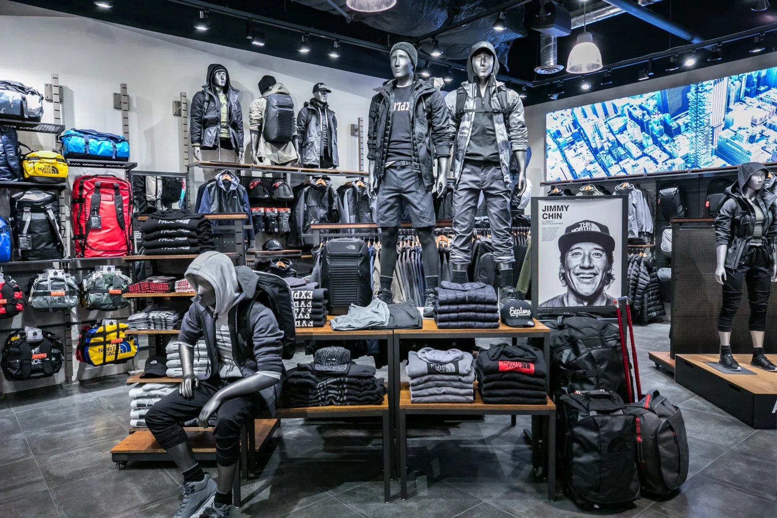 The North Face store interior displaying outdoor clothing, backpacks, folded apparel, mannequins, and a Jimmy Chin poster.