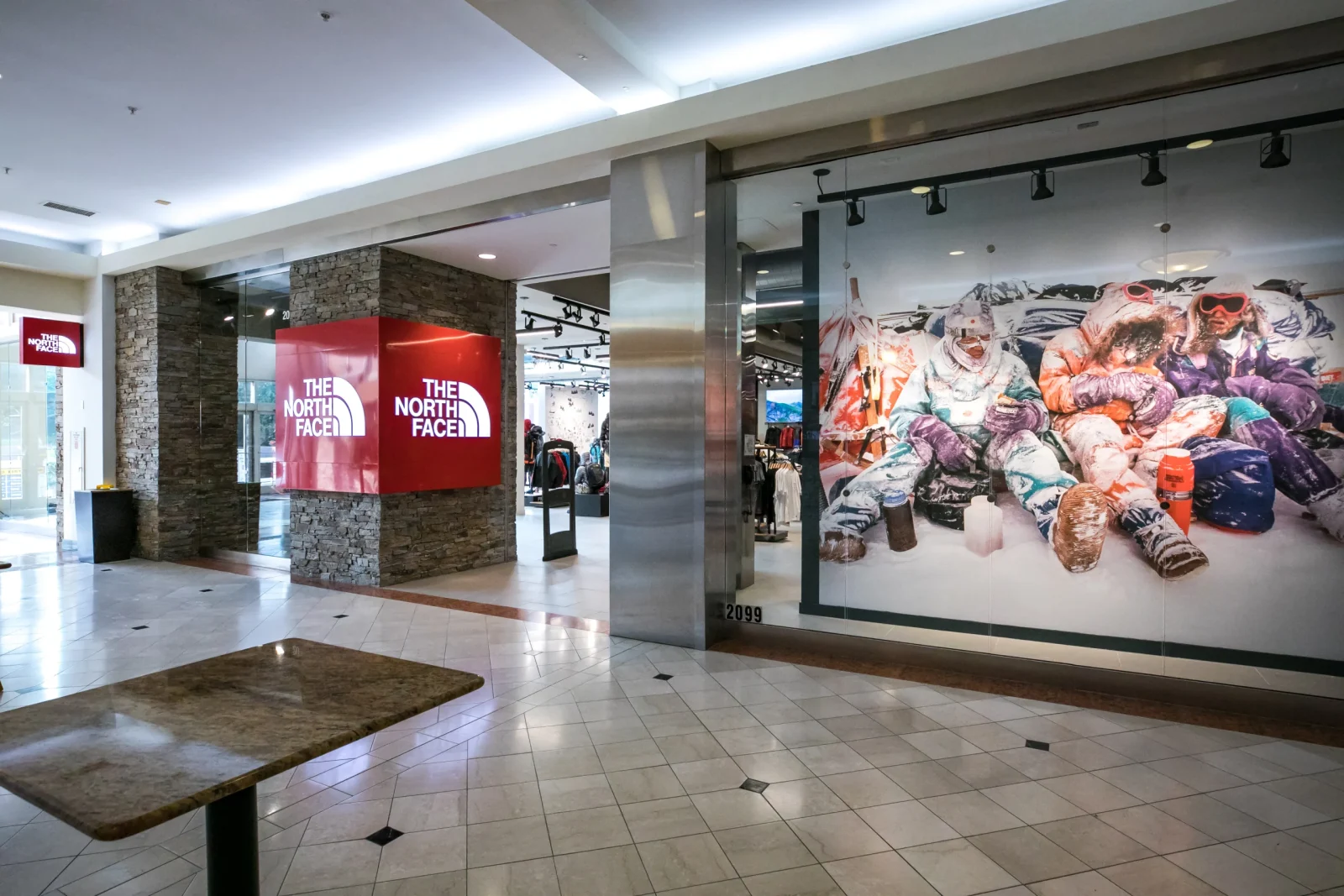 The North Face storefront in a shopping mall, with red illuminated logos and a colorful mural of winter athletes in the window.