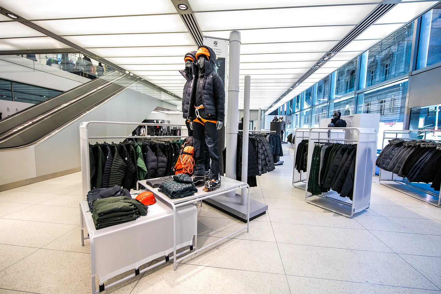Outdoor apparel store display with a mannequin in mountaineering gear surrounded by jackets, clothing racks, and folded garments