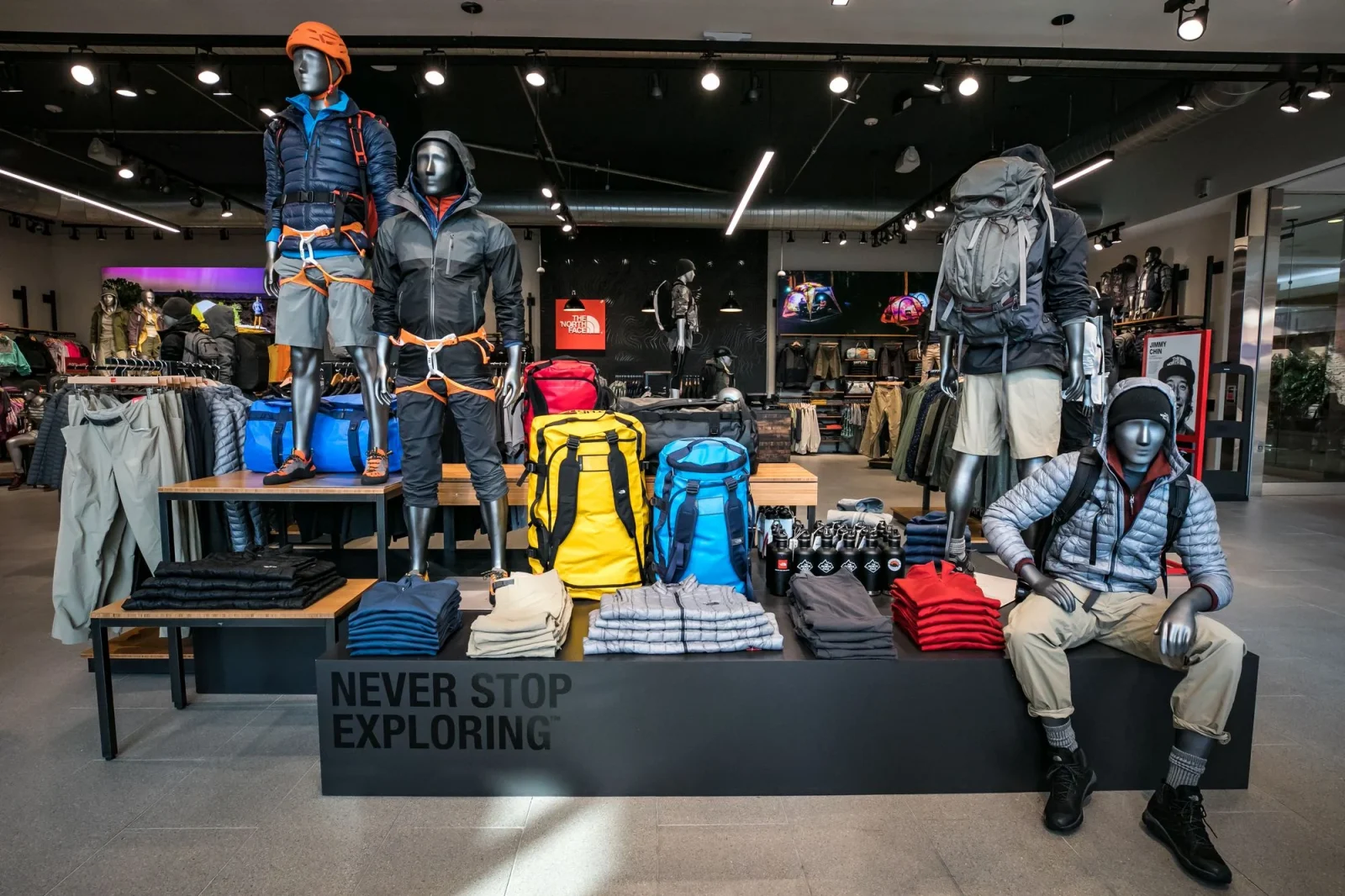 Outdoor apparel store display with mannequins in hiking gear, backpacks, clothing, and a “Never Stop Exploring” sign.