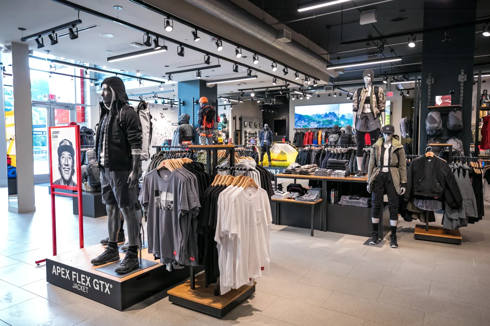 Outdoor apparel store interior with mannequins, clothing racks, and an Apex Flex GTX jacket display.