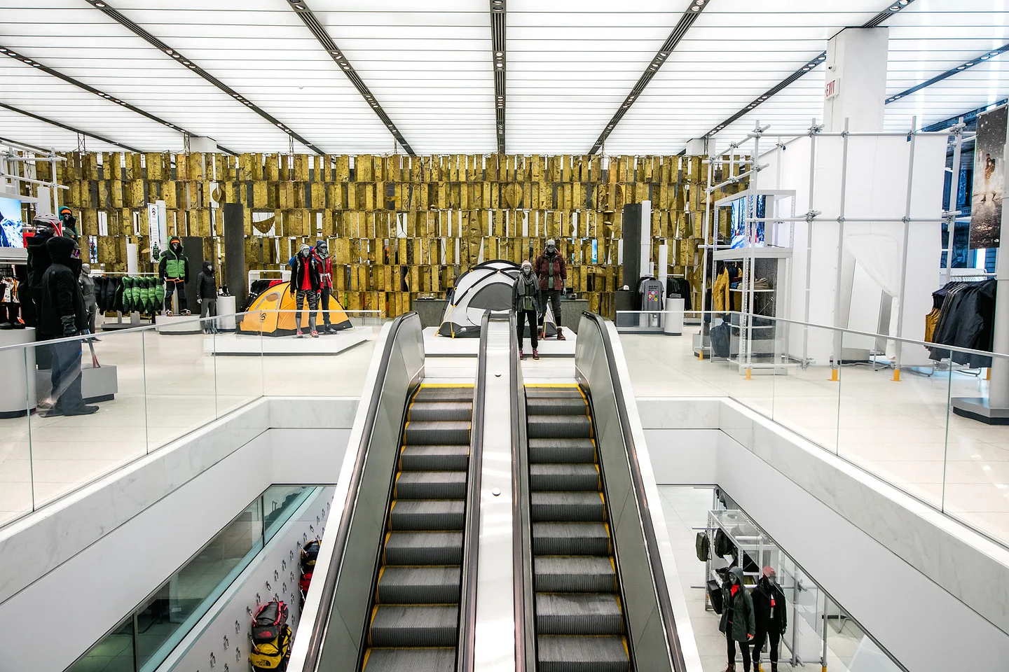 Outdoor apparel store interior with escalators, mannequins, tents, and climbing gear displays.