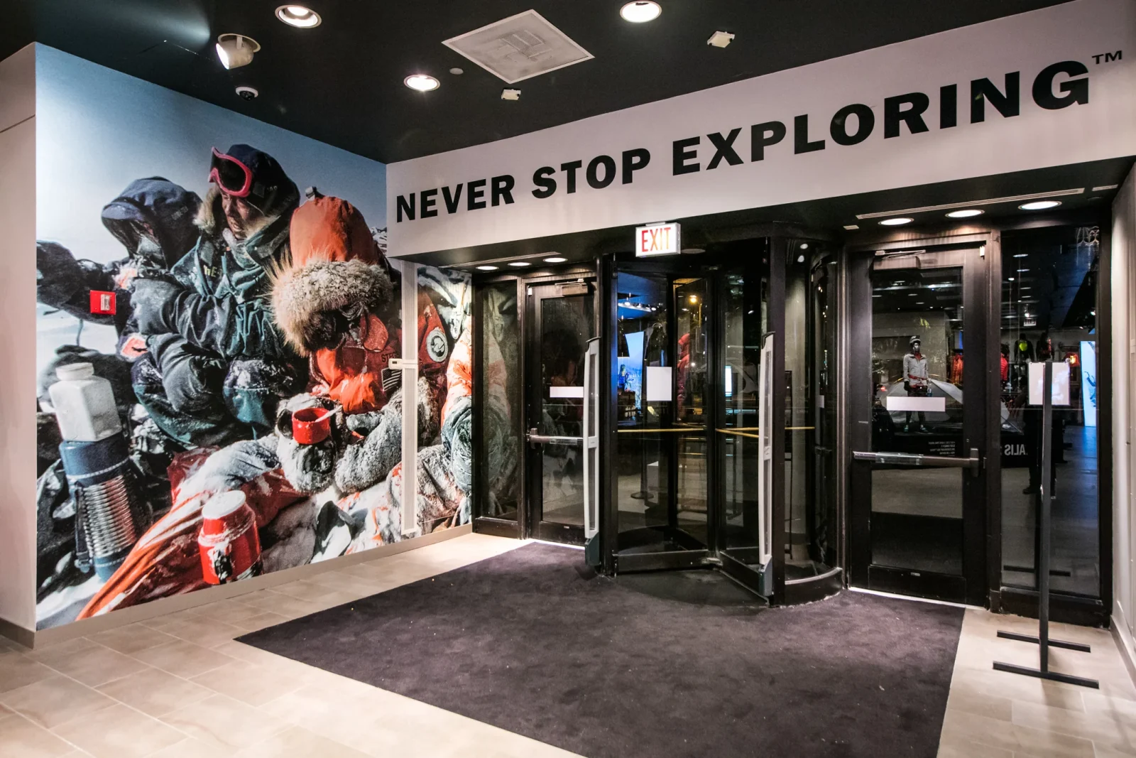 Outdoor retail store entrance with a mountain expedition mural and the words “NEVER STOP EXPLORING” above the doors.