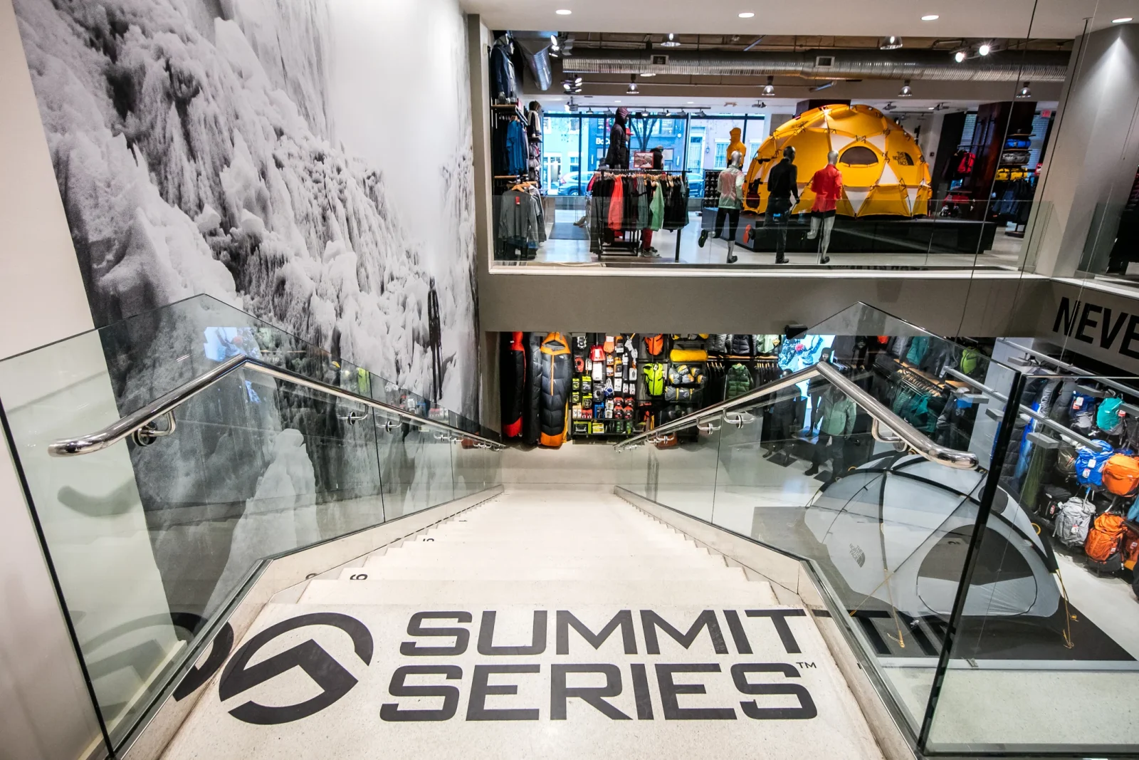 Outdoor apparel store interior with a yellow tent display, mannequins, gear, and “SUMMIT SERIES” lettering on the staircase.