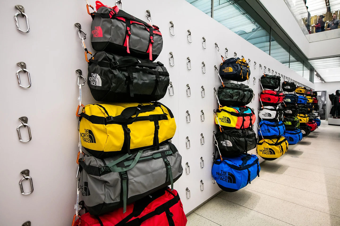 Colorful The North Face duffel bags displayed on a wall with climbing carabiners