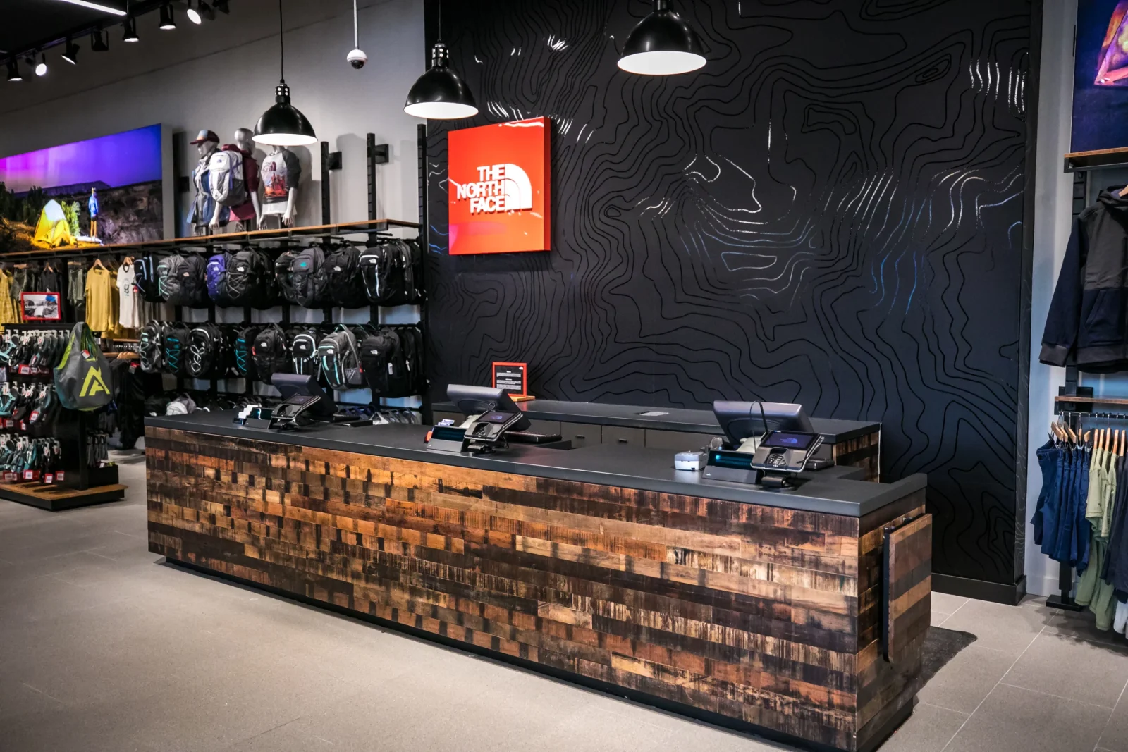 Interior of a The North Face store with clothing and backpacks displayed around a wood-front checkout counter.