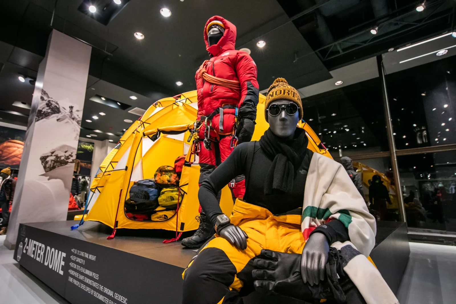 Store display featuring a yellow two-meter dome tent and mannequins dressed in mountaineering gear.