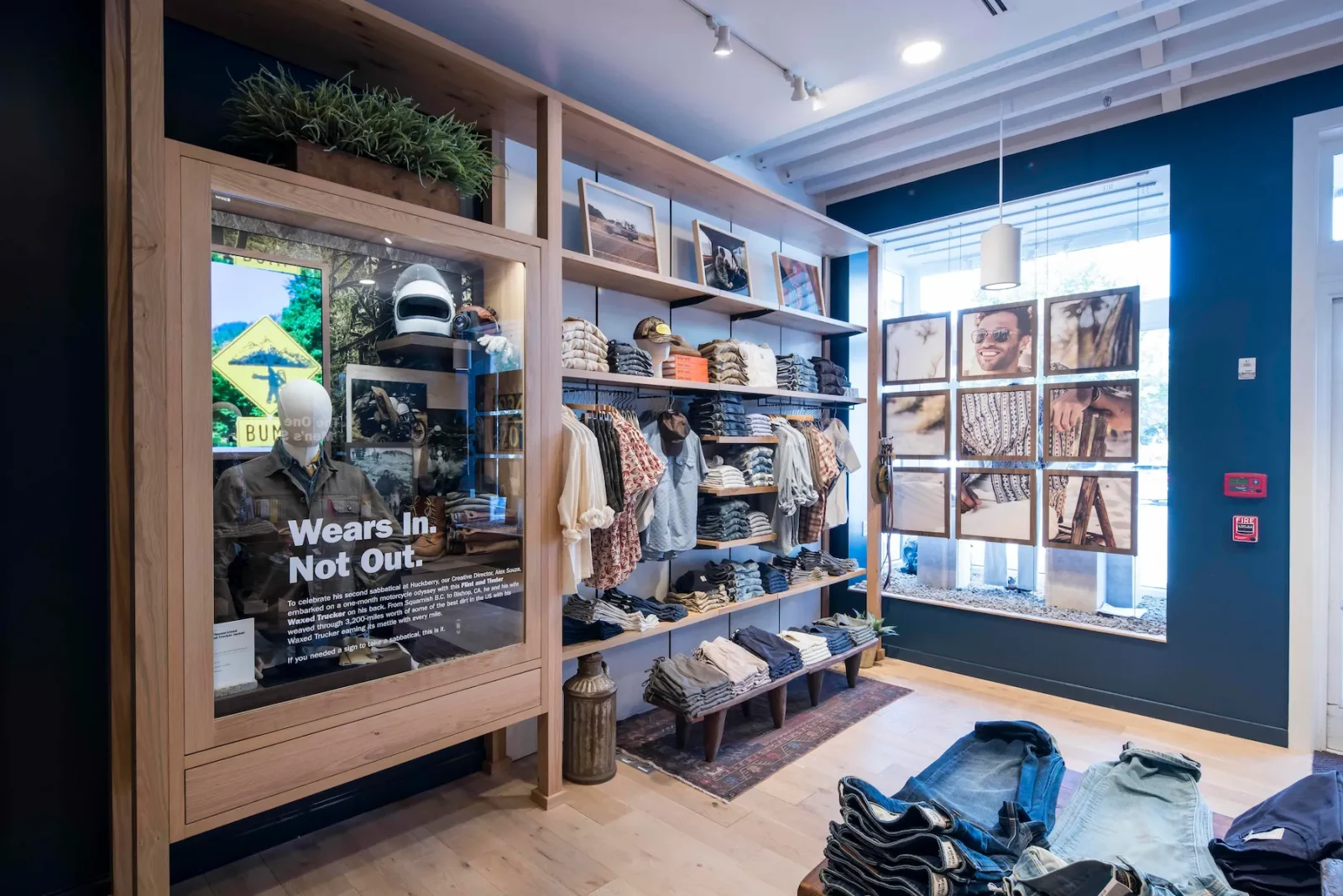 Huckberry retail interior with shelves of clothing, framed outdoor photography, and a display reading “Wears In. Not Out.”