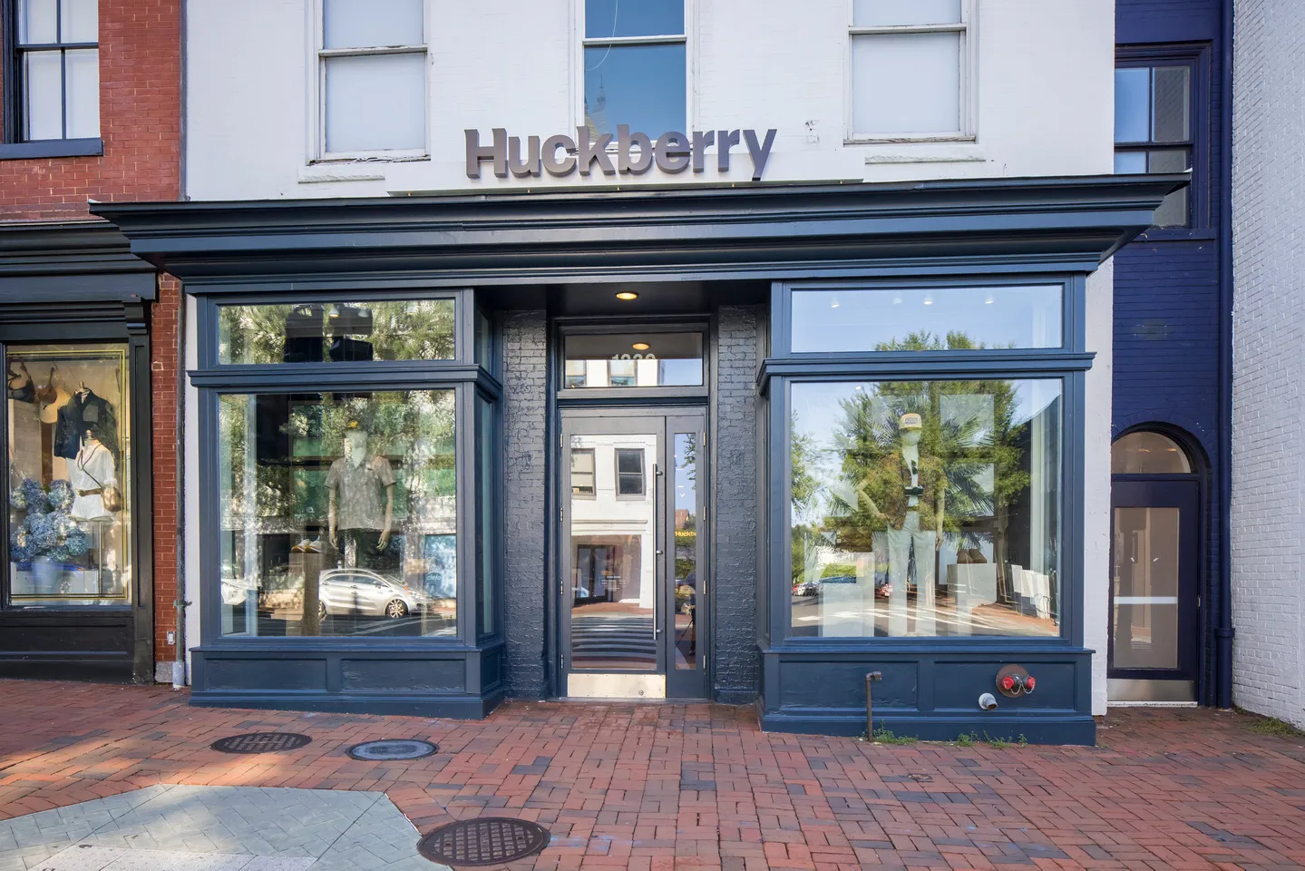 Huckberry storefront with dark blue trim, large display windows, mannequins, and Huckberry sign above the entrance