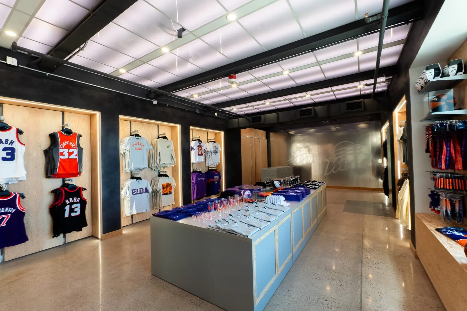 Interior of a Phoenix Suns team store displaying jerseys, shirts, hats, drinkware, and other basketball merchandise.