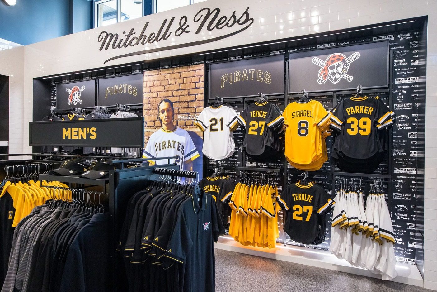 Pittsburgh Pirates team store display with Mitchell & Ness sign, jerseys, caps, and men's clothing in black, gold, and white