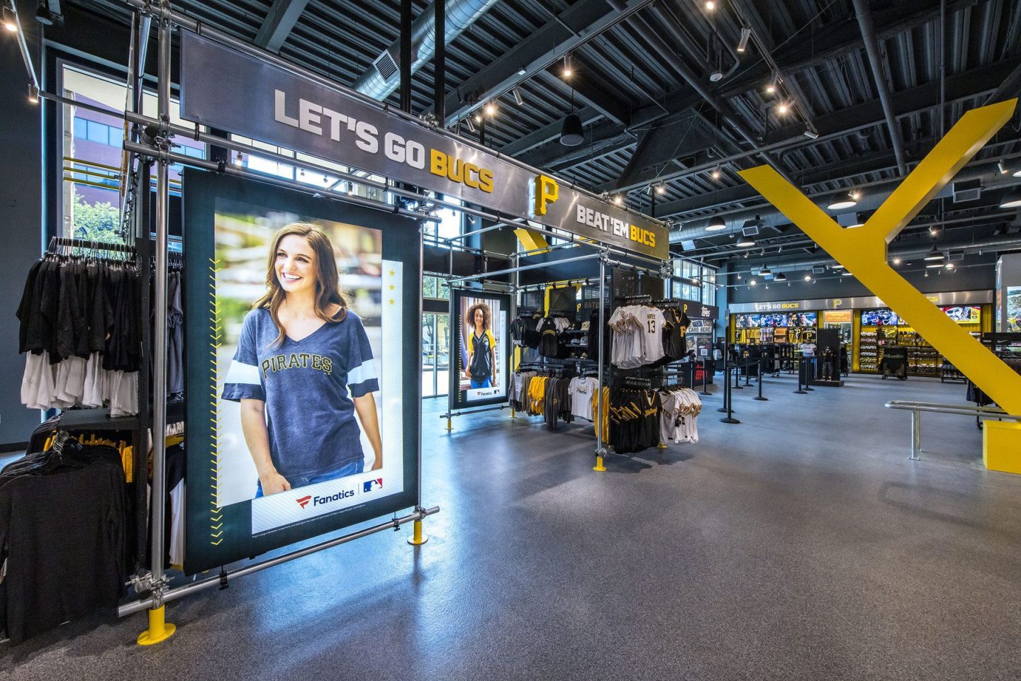 Interior of a Pittsburgh Pirates team store displaying apparel, merchandise, and signs reading “LET’S GO BUCS” and “BEAT ’EM BUCS.”