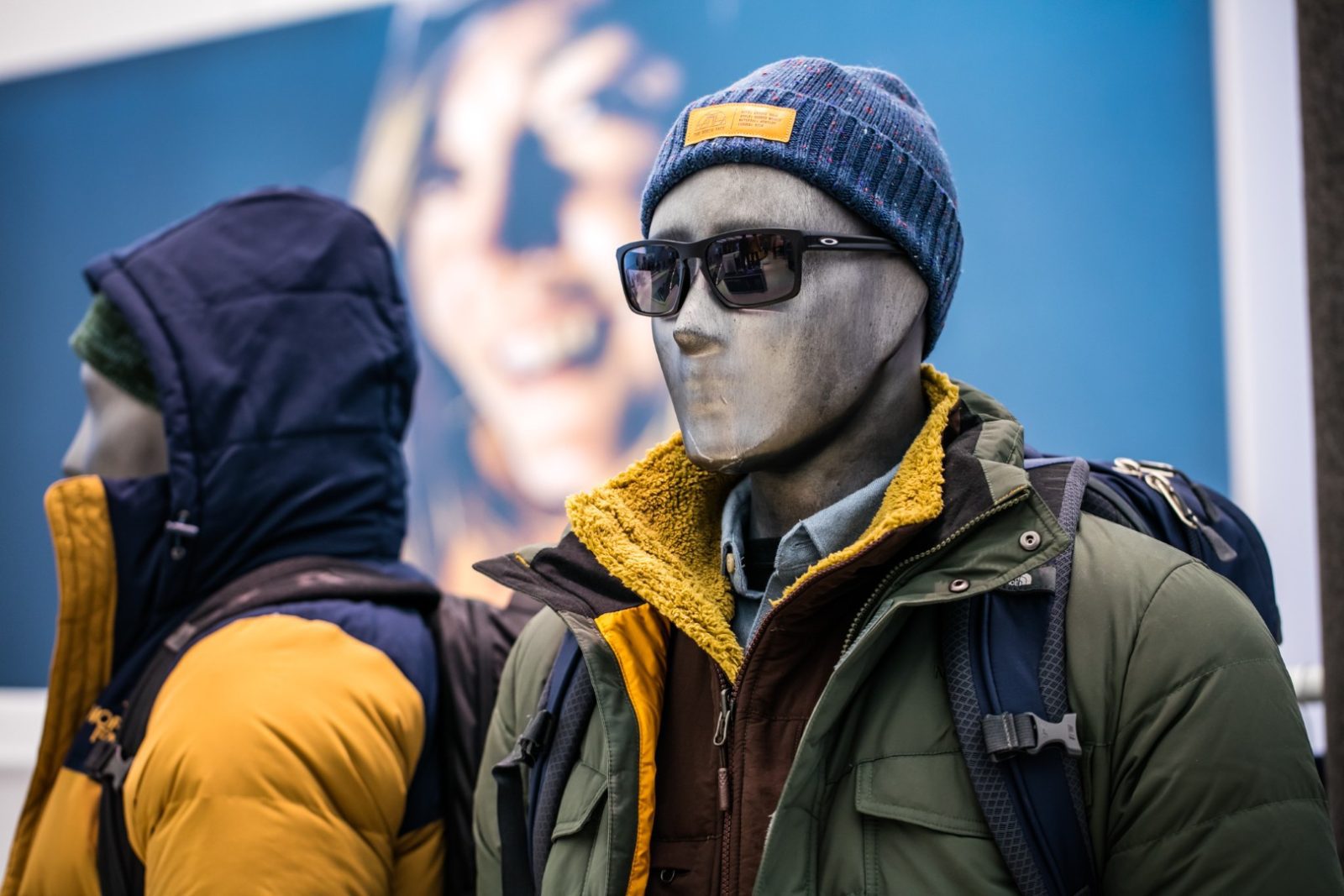 Mannequins wearing layered outdoor clothing, sunglasses, beanies, and backpacks in a retail display