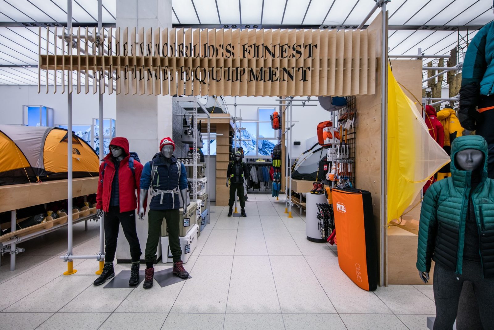 Outdoor gear store interior with mannequins, tents, climbing equipment, and a sign reading “The world’s finest equipment.”