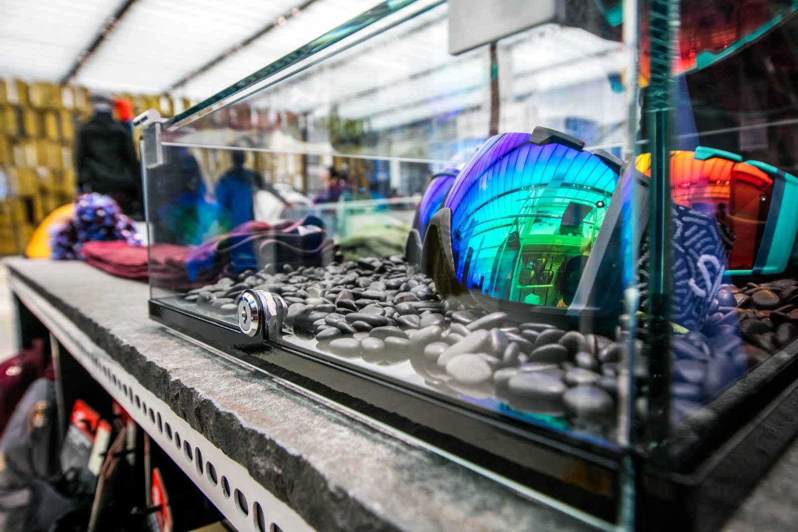 Colorful outdoor gear displayed behind glass on a bed of smooth stones