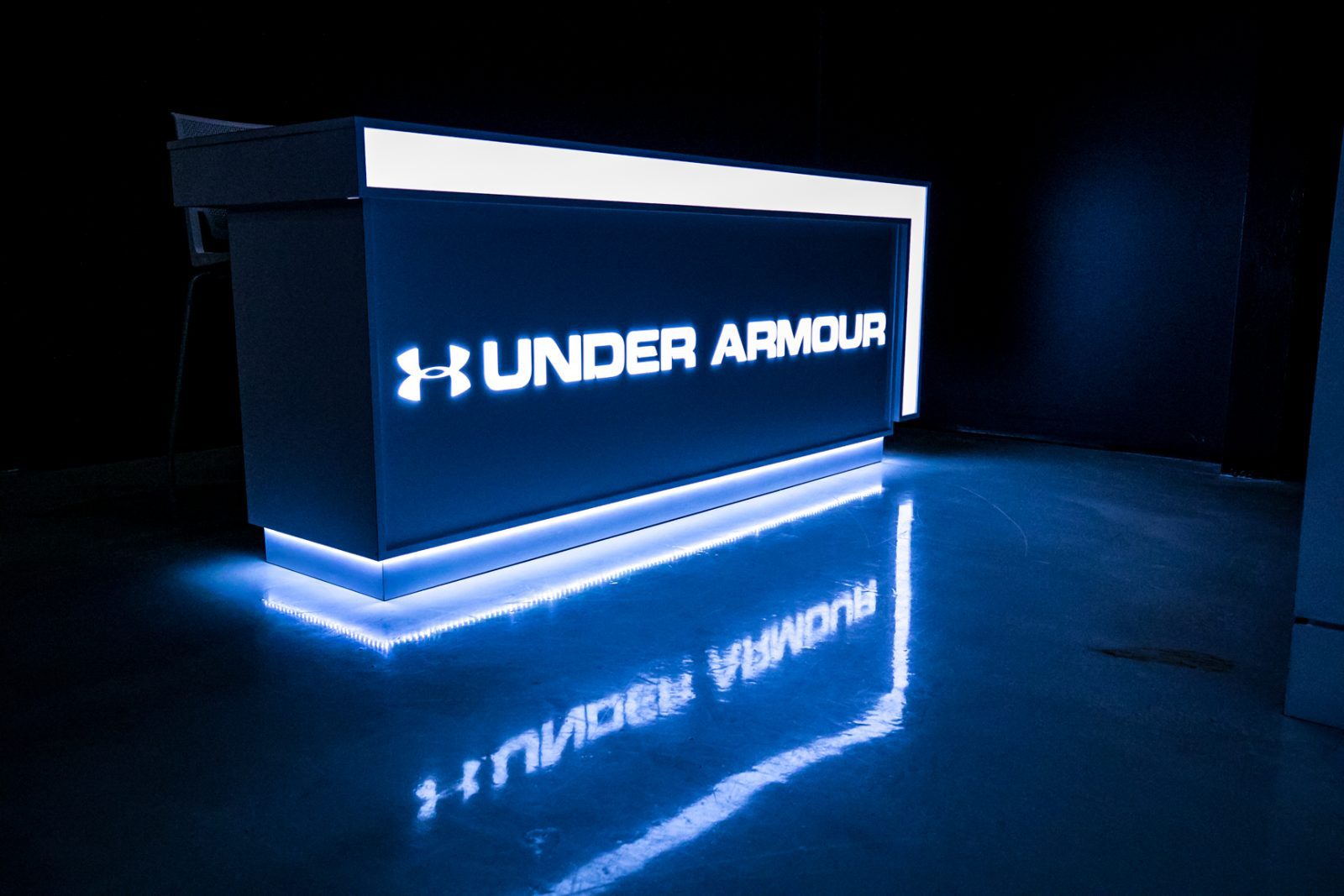 Illuminated Under Armour reception counter with glowing logo and blue-lit floor