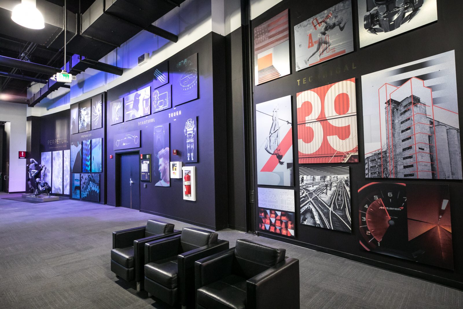Modern showroom lounge with black leather chairs and walls covered in sports, technology, and architectural artwork