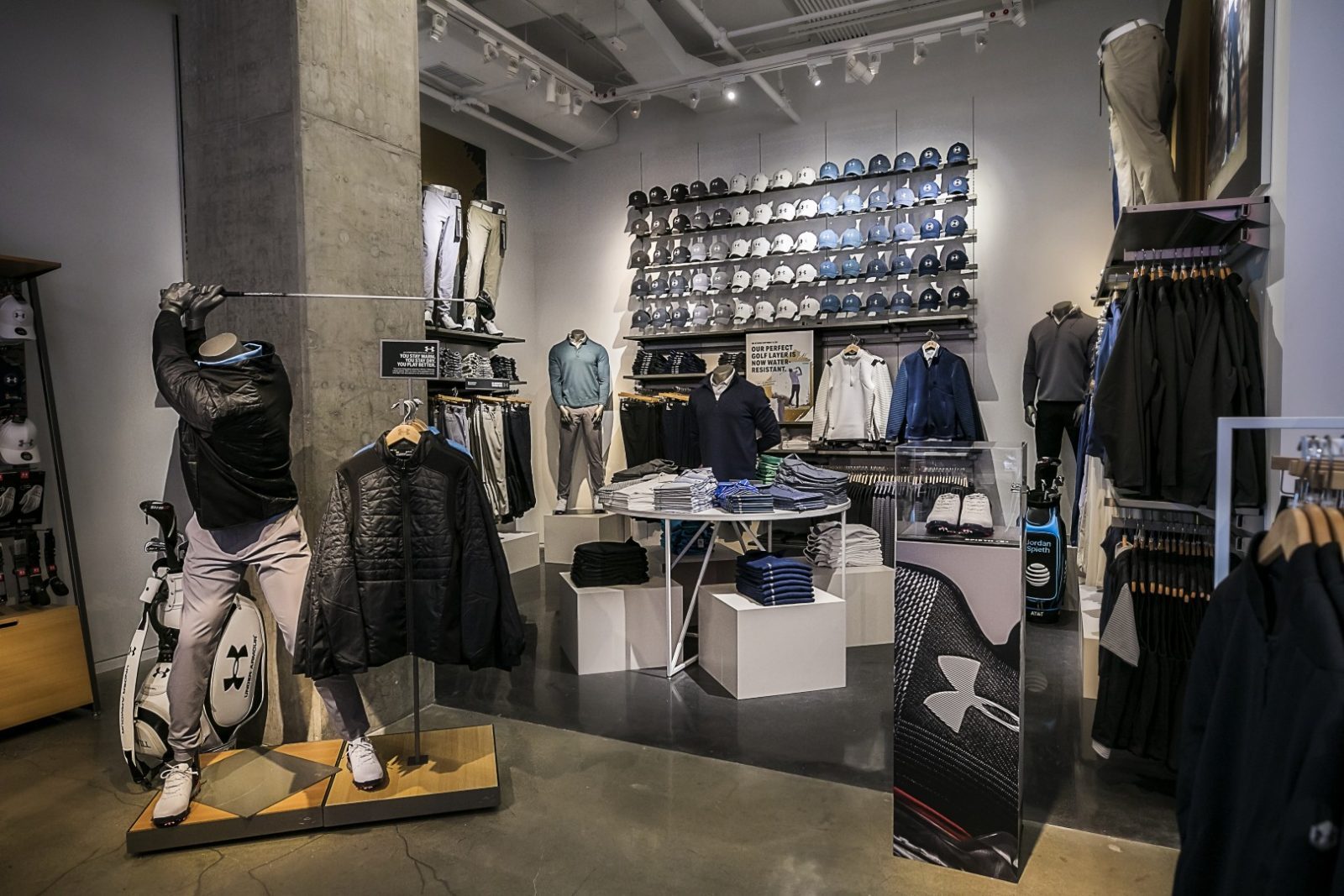 Under Armour golf apparel store interior with mannequins, clothing displays, golf bags, and a wall of caps