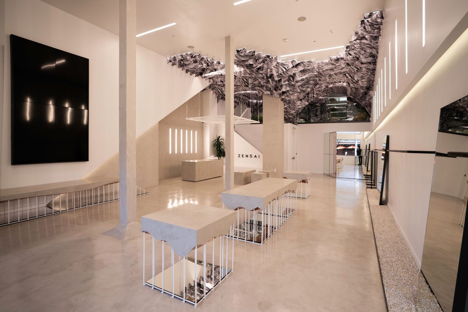 Interior of Zensai featuring a minimalist cream-colored space, sculptural black-and-white ceiling installation, tables, and the ZENSAI wall sign.