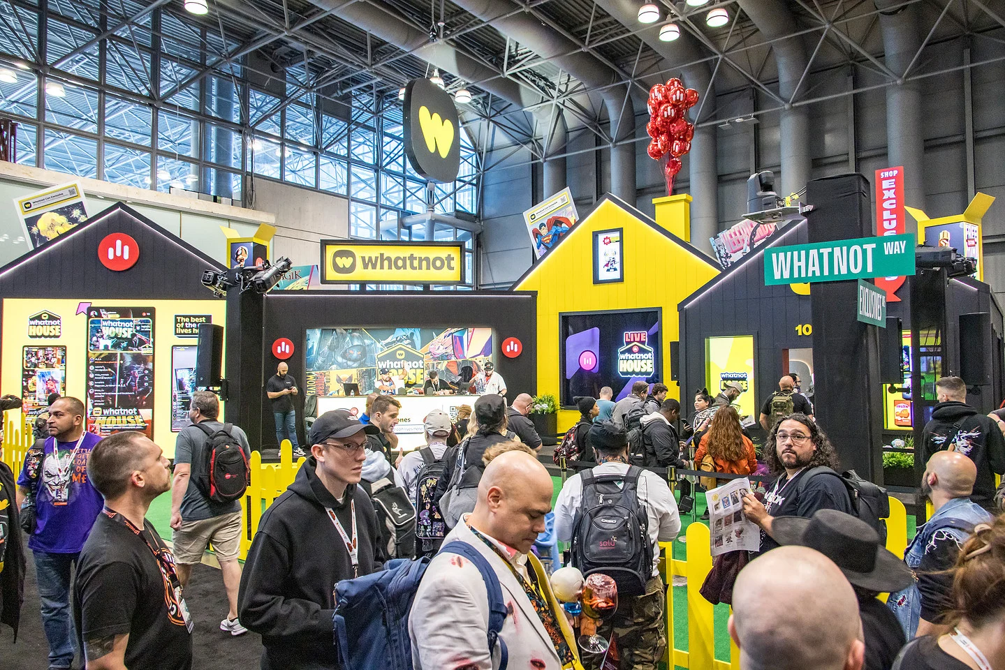Crowded Whatnot convention booth featuring Whatnot House displays, branded storefronts, and yellow-and-black event decor.