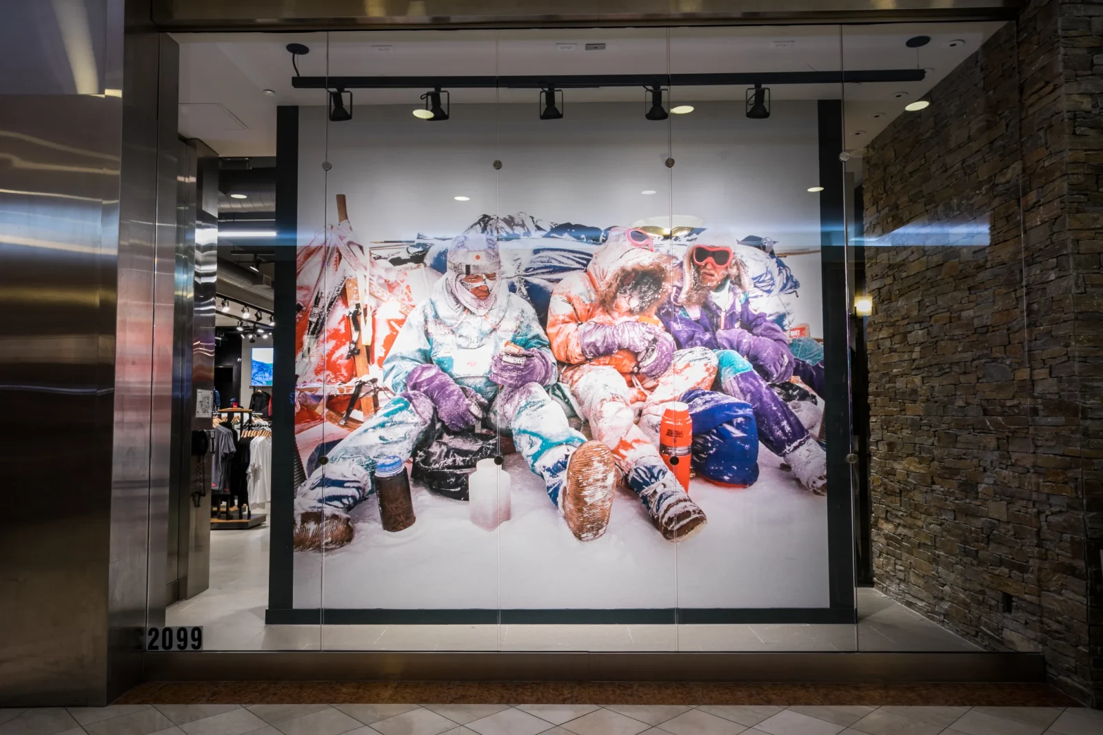 Storefront display featuring a colorful mural of people in winter gear seated in the snow, with clothing racks visible inside