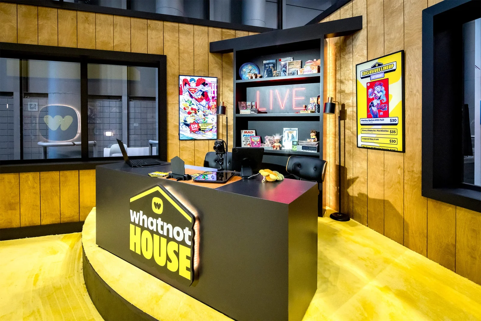 Whatnot House reception desk with branded sign, merchandise shelves, and an exclusive live lineup poster